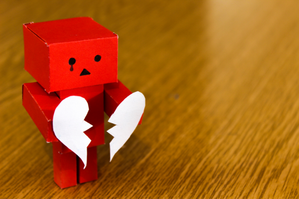 красный картонный человечек держит разбитое сердце